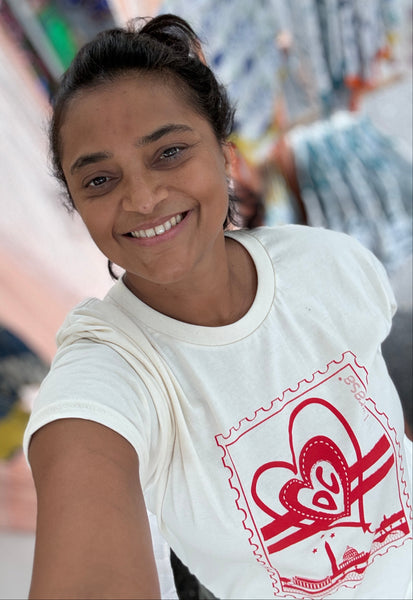 A smiling woman taking a selfie while wearing a white t-shirt with a red heart and stamp graphic design.